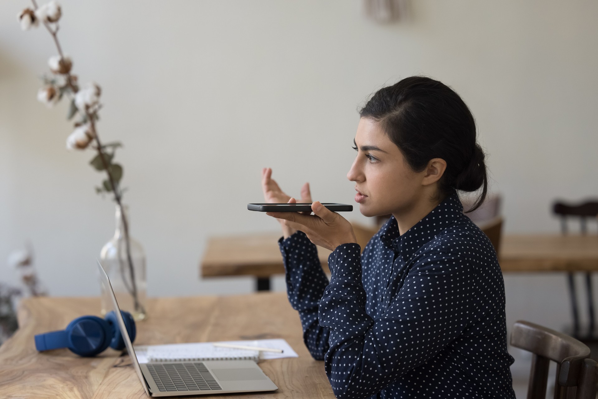 Serious focused Indian woman holds smartphone lead talk on speakerphone